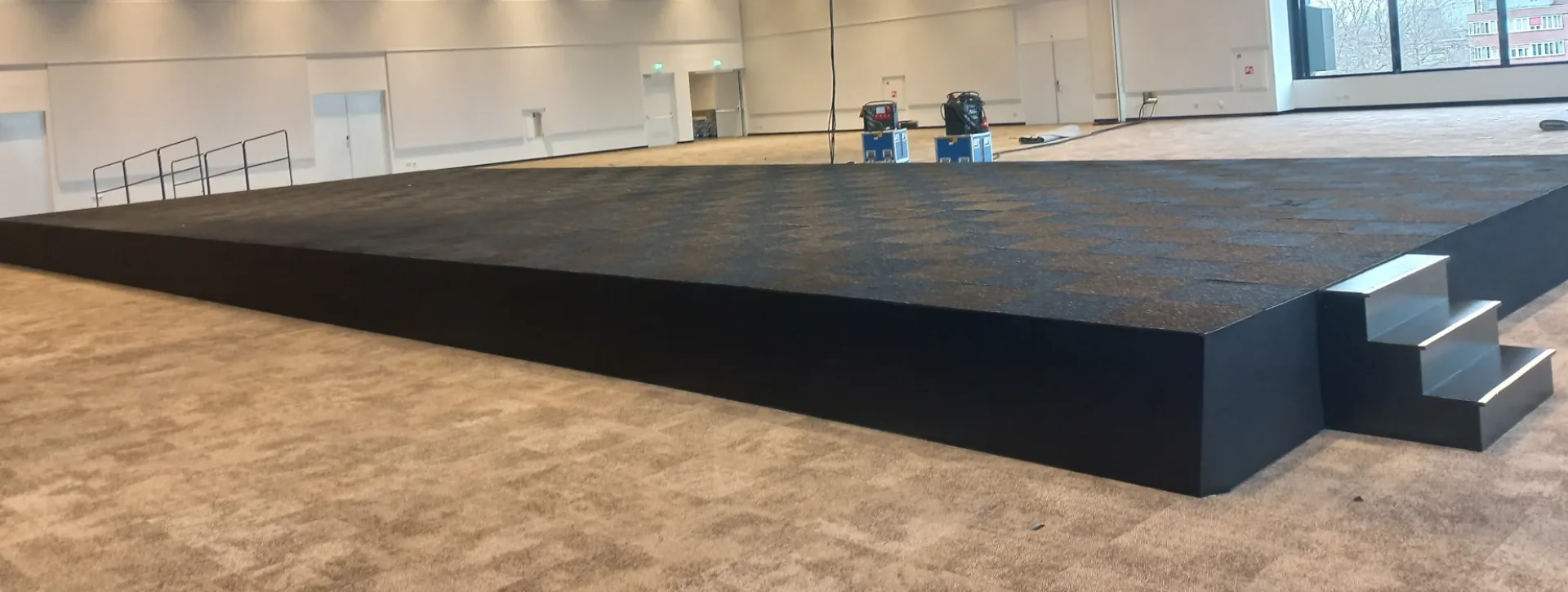 Groot podium met zwarte podiumrok en trap in een zaal met vloerbedekking