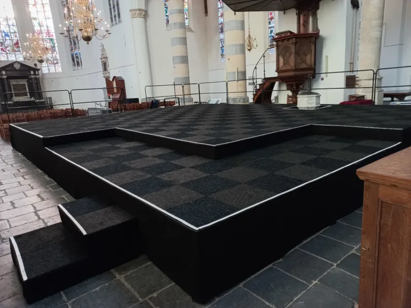 Podium met verschillende lagen met zwarte rok en vloertegels in Delftse kerk